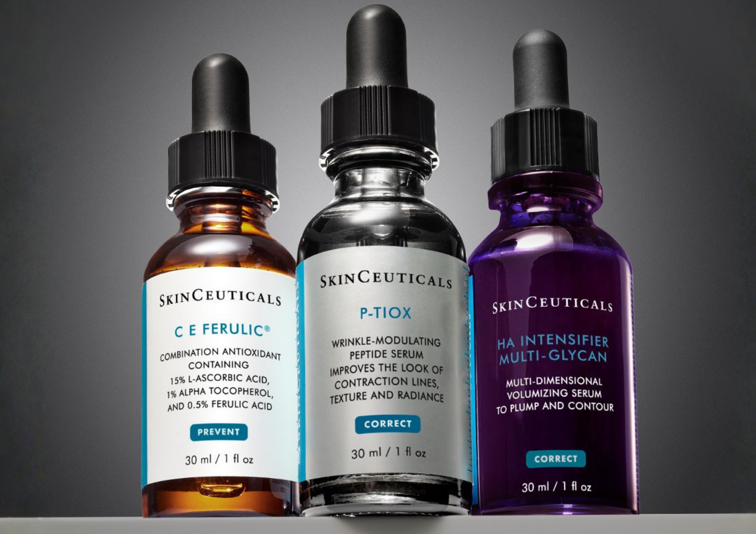 Three SkinCeuticals serum bottles lined up: orange, clear, and purple with droppers against a gray gradient background, label text visible (50+ ml).